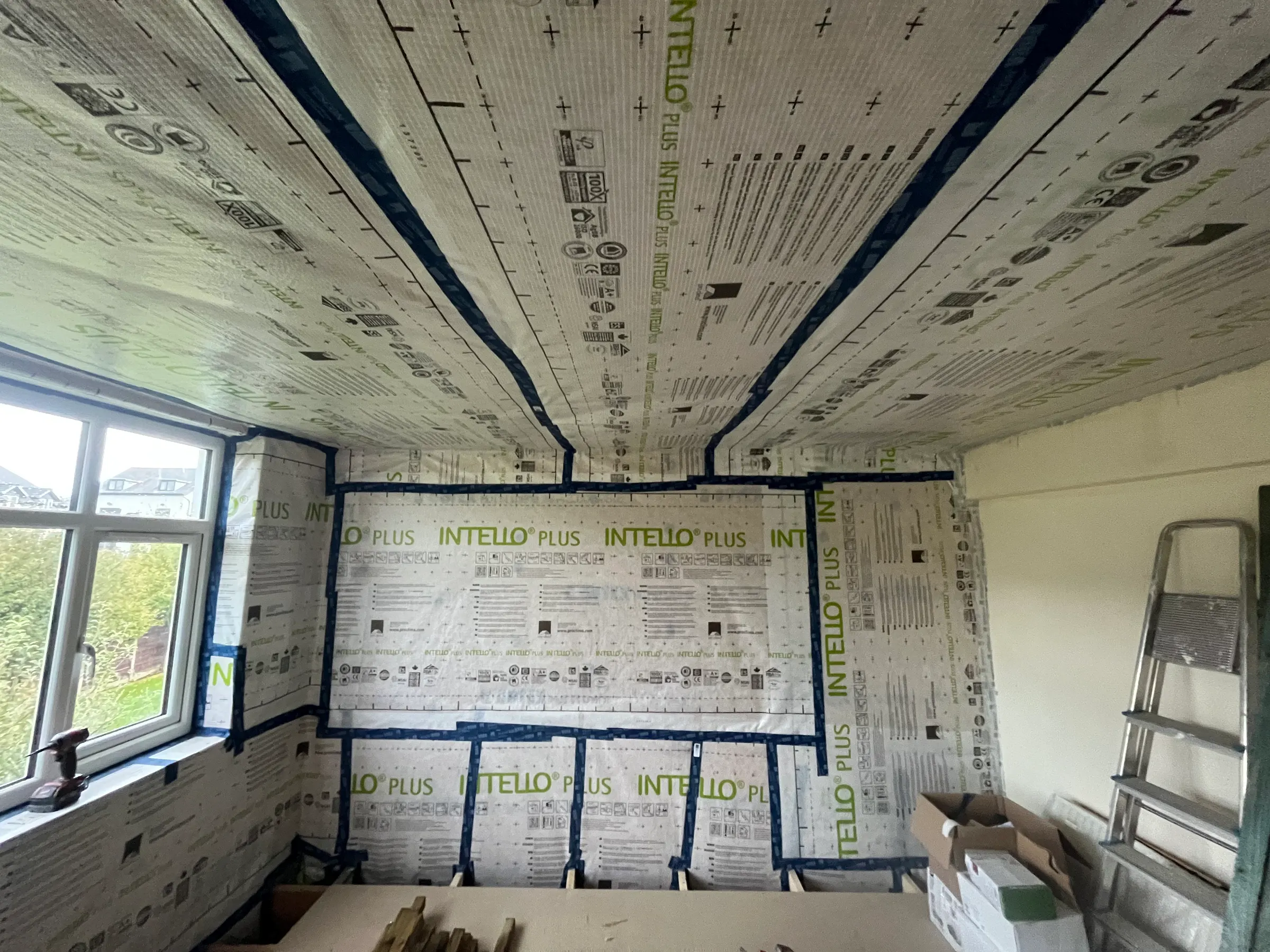 Airtightness membrane being taped out across a wall and ceiling